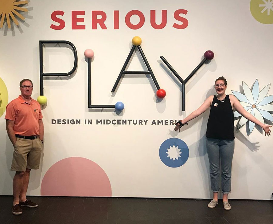 Man and young woman in front of Serious Play exhibition with the words Serious Play on the wall behind them