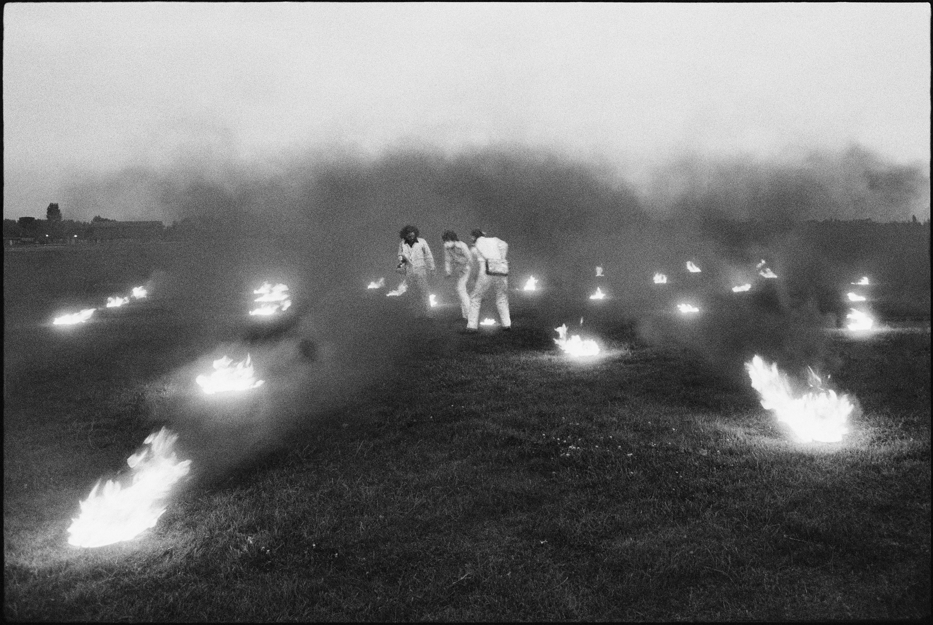 Black and white photo of field with lit fires