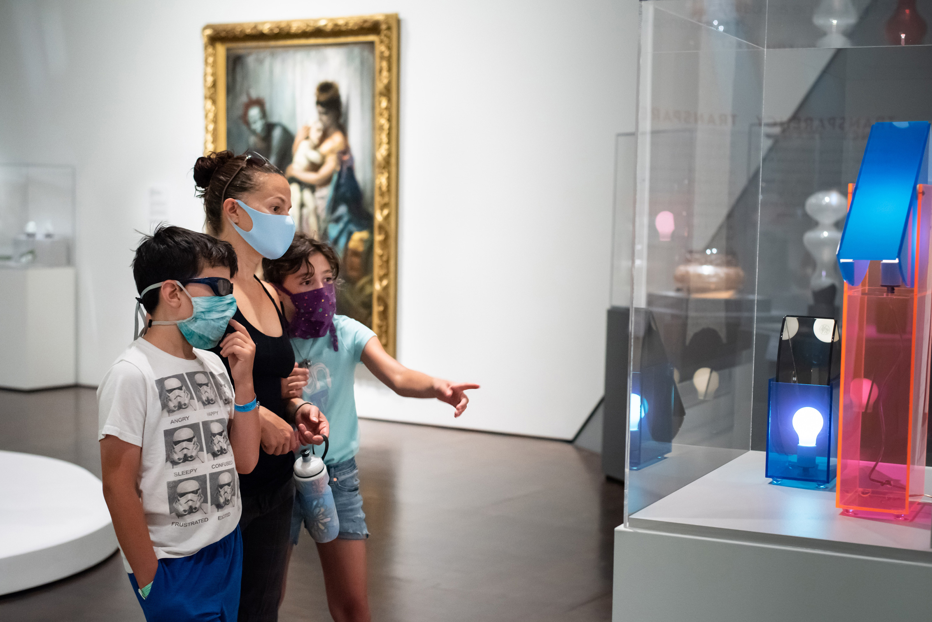 Masked mother looking at art with her two children
