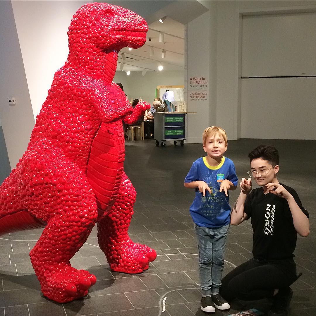 Two kids posing next to large red dinosaur sculputre