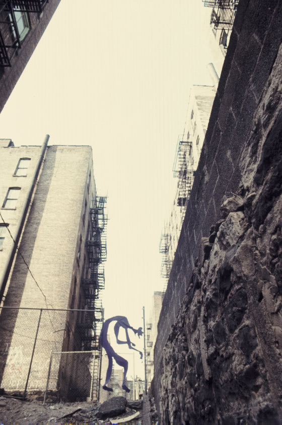 Photograph of large figure made of thin purple flag fabric hung in a street alleyway.
