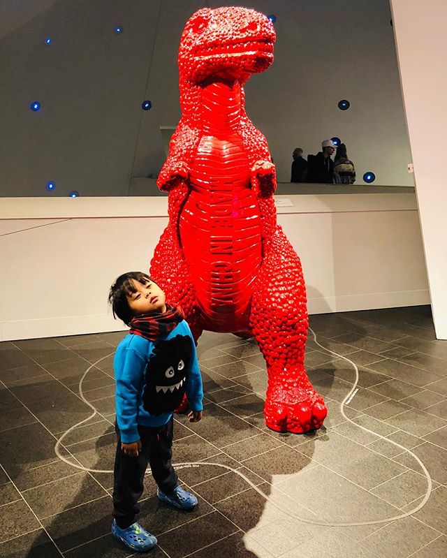Kid posing in front of red dinosaur sculpture