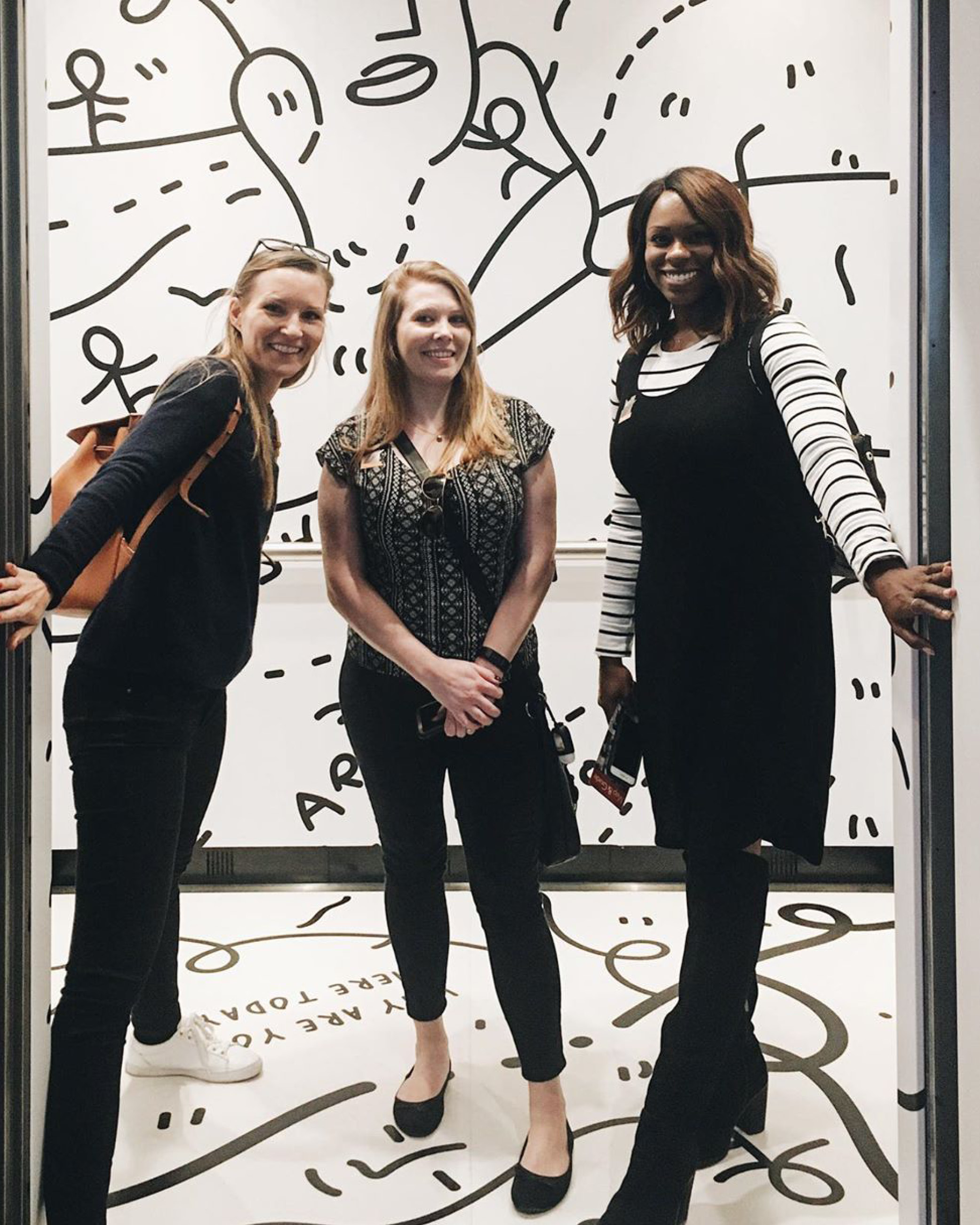 Three visitors looking out from inside an elevator that is part of the Shantell Martin exhibition