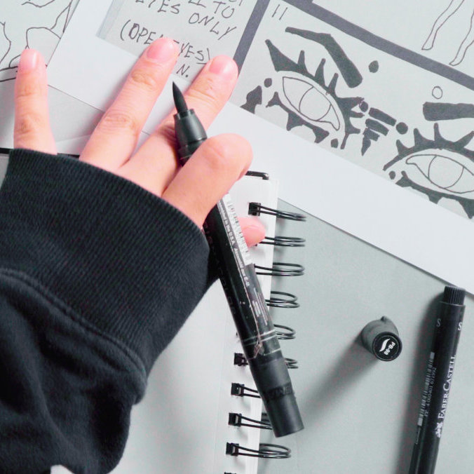 Photo of a hand holding a pen, and a table full of storyboard-style illustrations