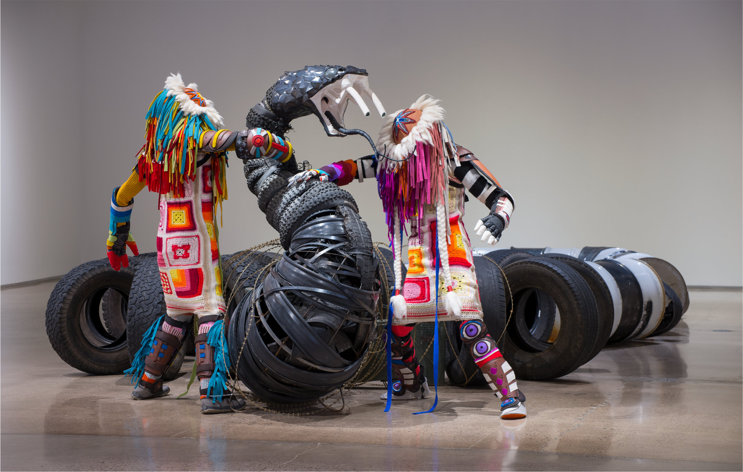 Large-scale sculptural installation made up of oil drums, ammunition cans, trash, and found objects arranged in a snake-like pattern.