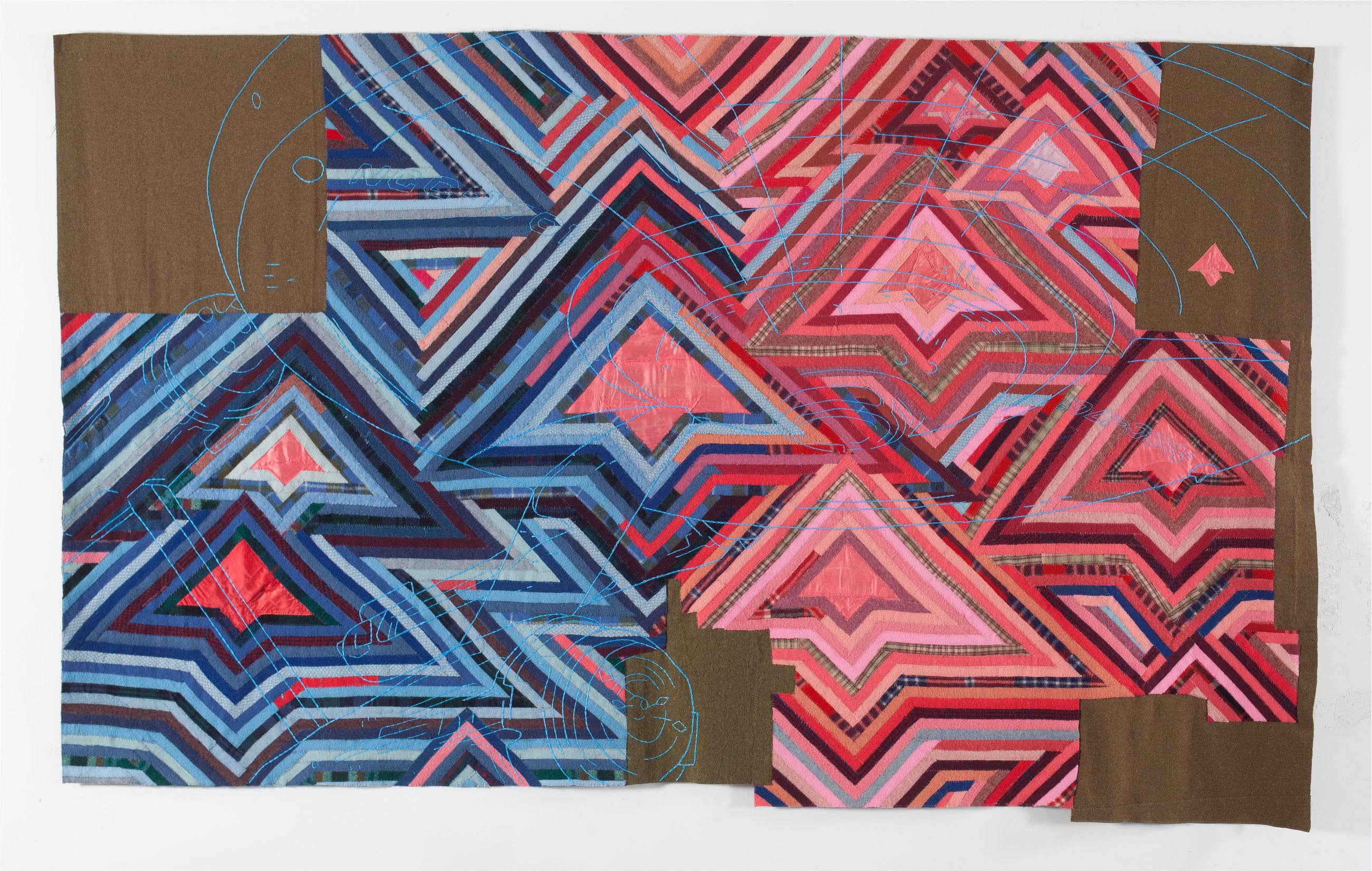 Large textile comprised of dozens of overlapping triangle patterns in red, pink, blue and purple. In the center, a blanket of silver tin jingles lays on top of the textile.