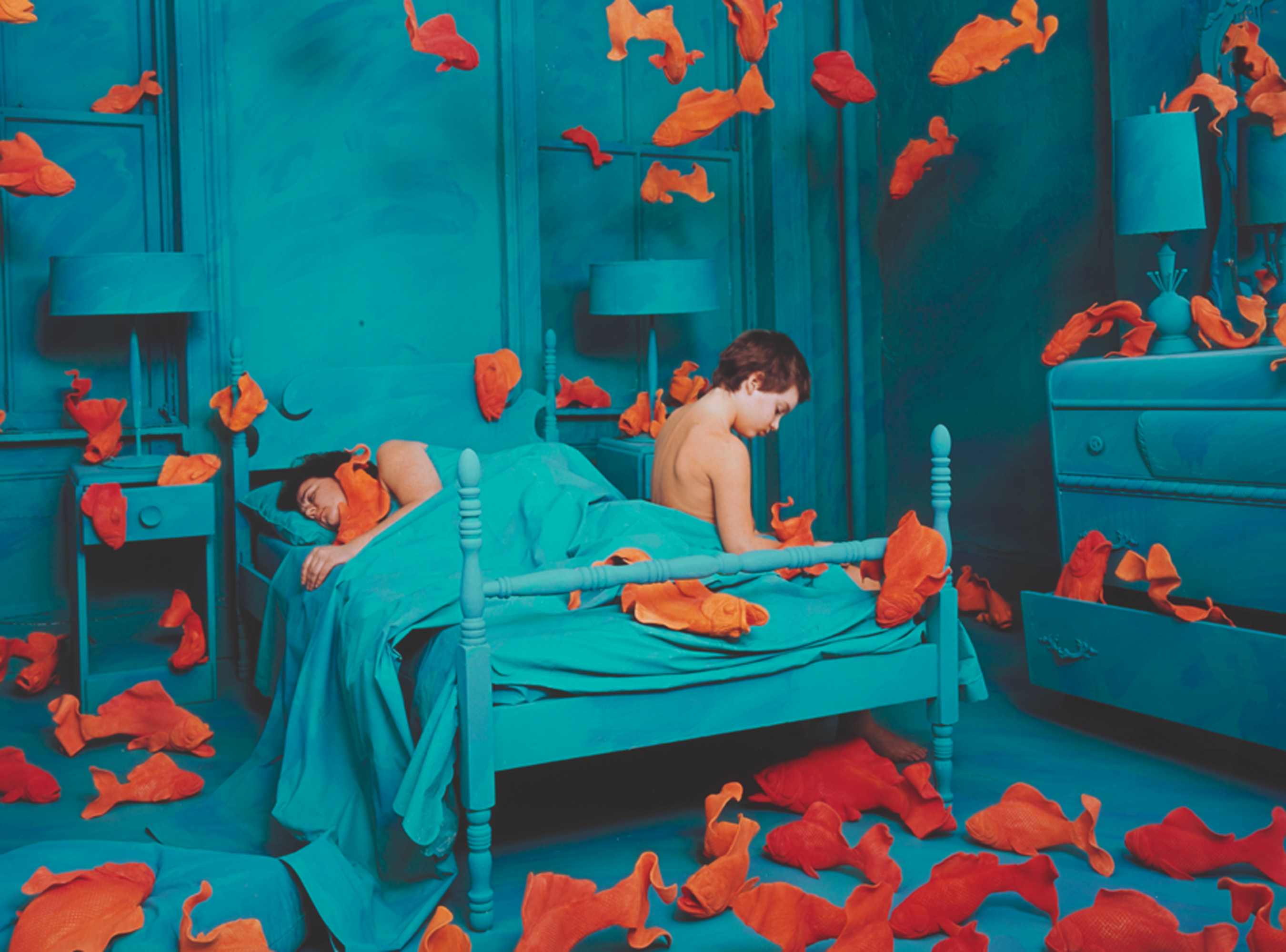 Surreal photograph of couple on a bed surrounded by orange fish