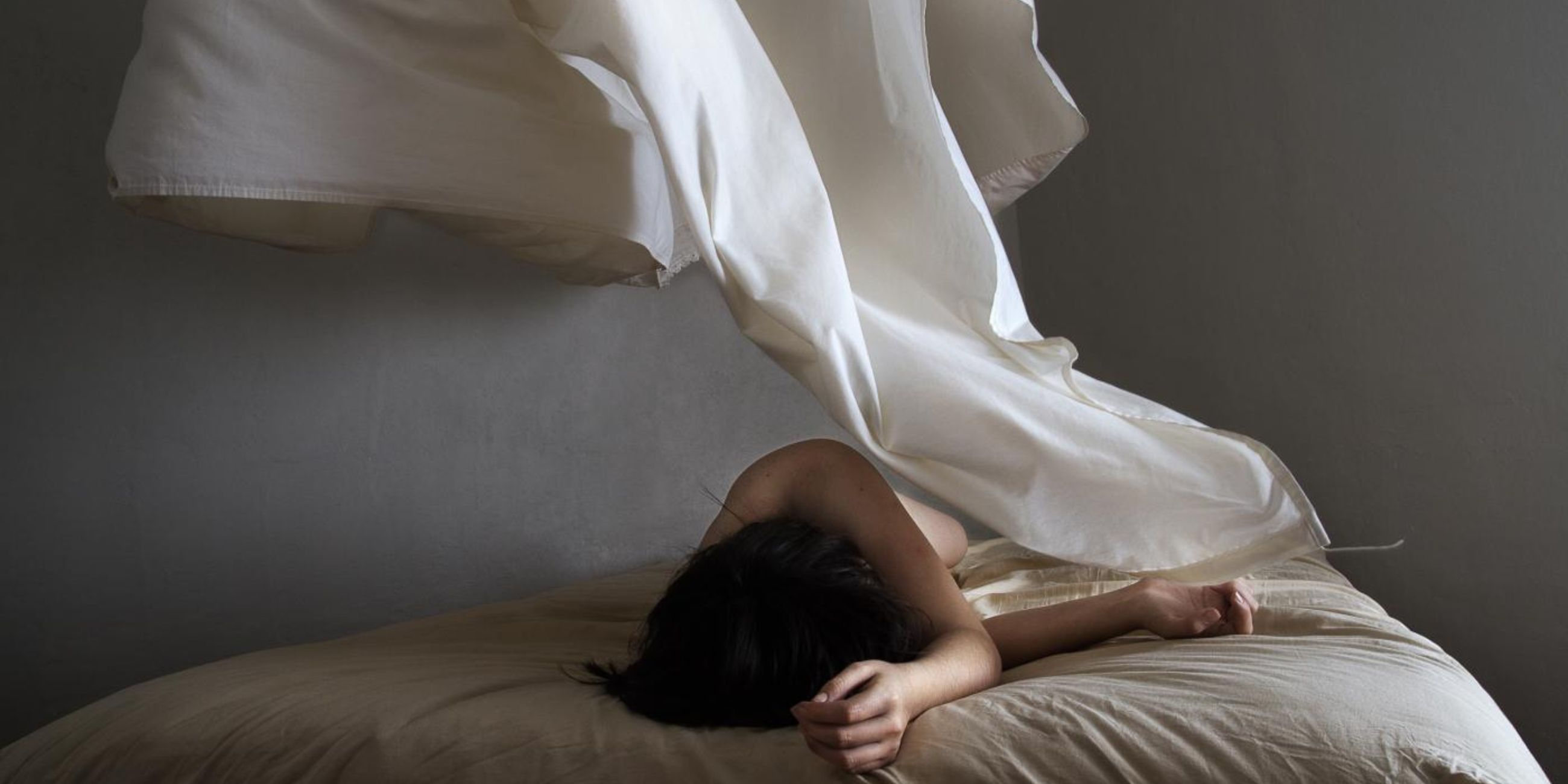 Photograph of a woman in a white dress laying in bed