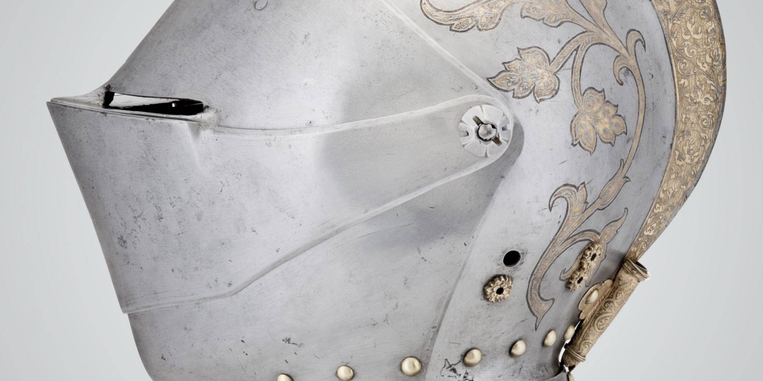 Profile view of a steel and brass tournament helmet that covers entire face and head