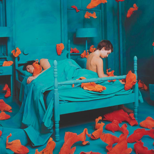 Surreal painting of a couple in bed surrounded by floating orange fish