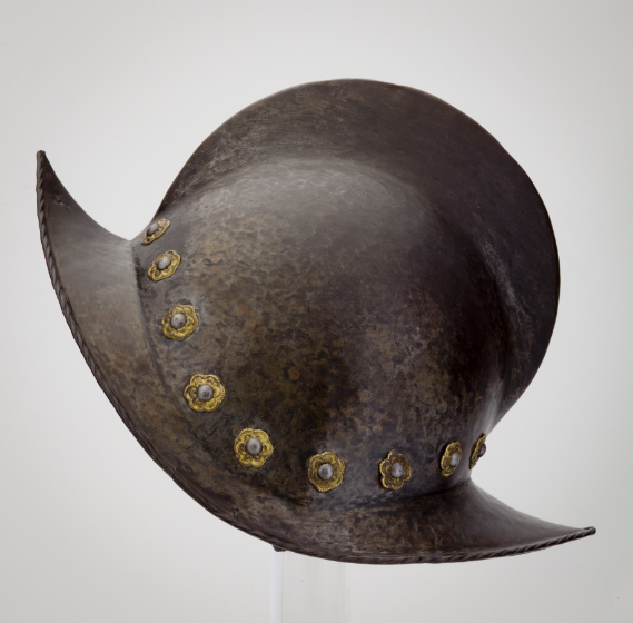 A metal helmet with a single fin-like ridge on top and a scalloped brim. It is decorated with gold flowers above the brim.