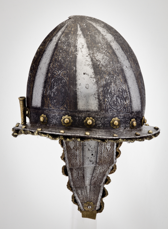 A metal helmet with an open face, short visor, leather chin strap, and three fin-like ridges running from the front to the back.