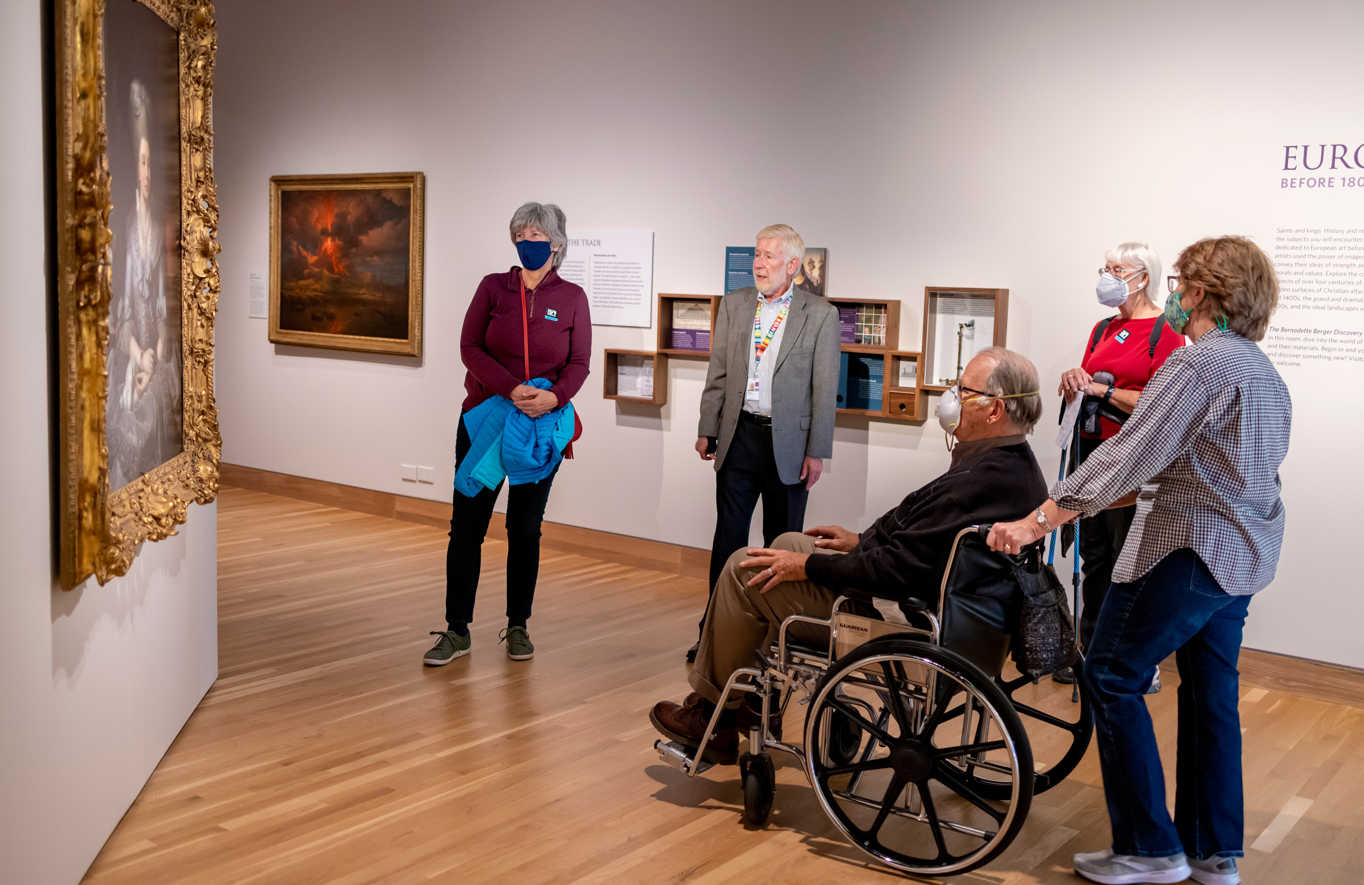 A man in a wheelchair and a group of other visitors listening to a docent on a collection tour