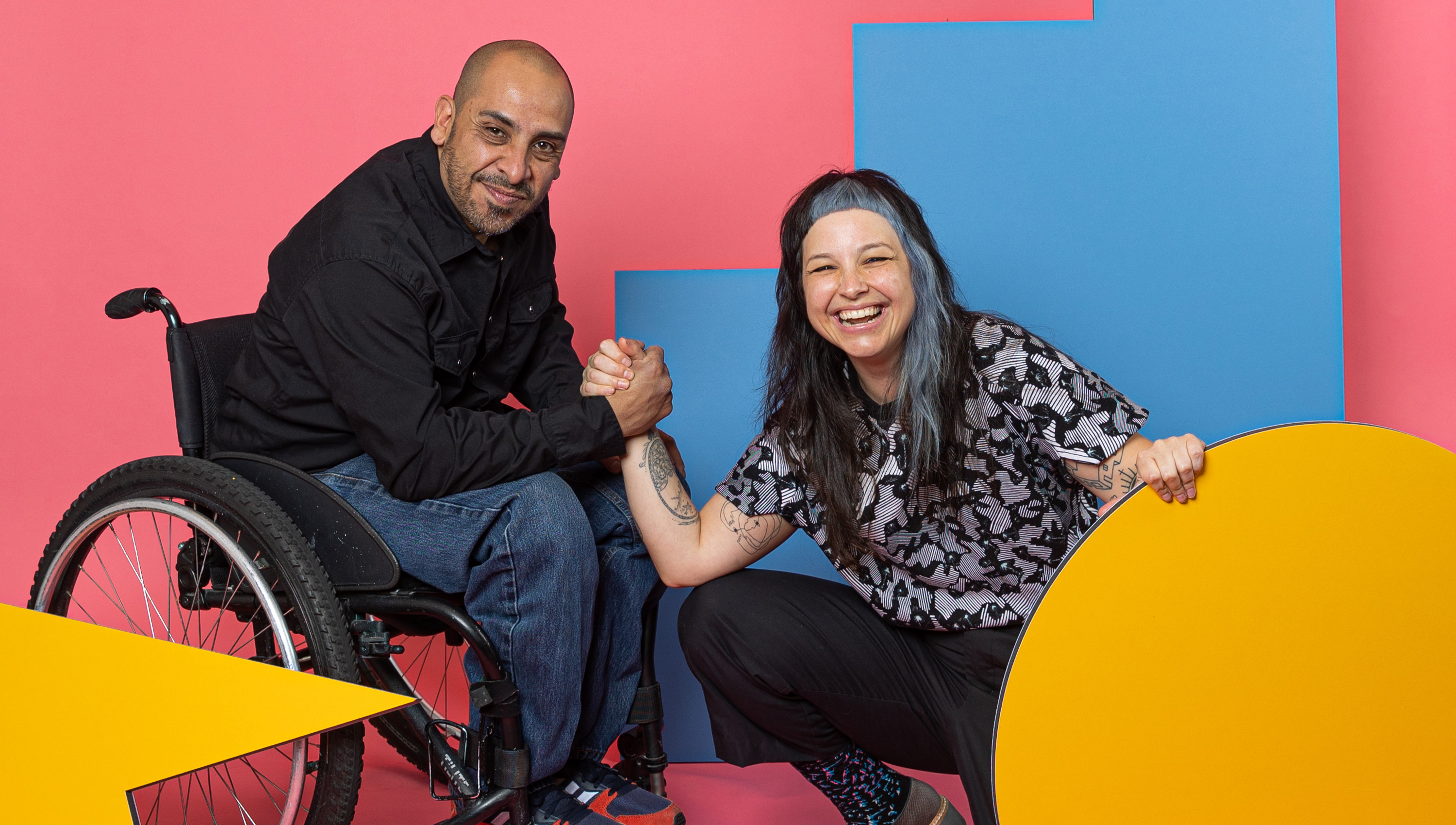 Sam and Javier smiling at camera surrounded by colorful shapes.