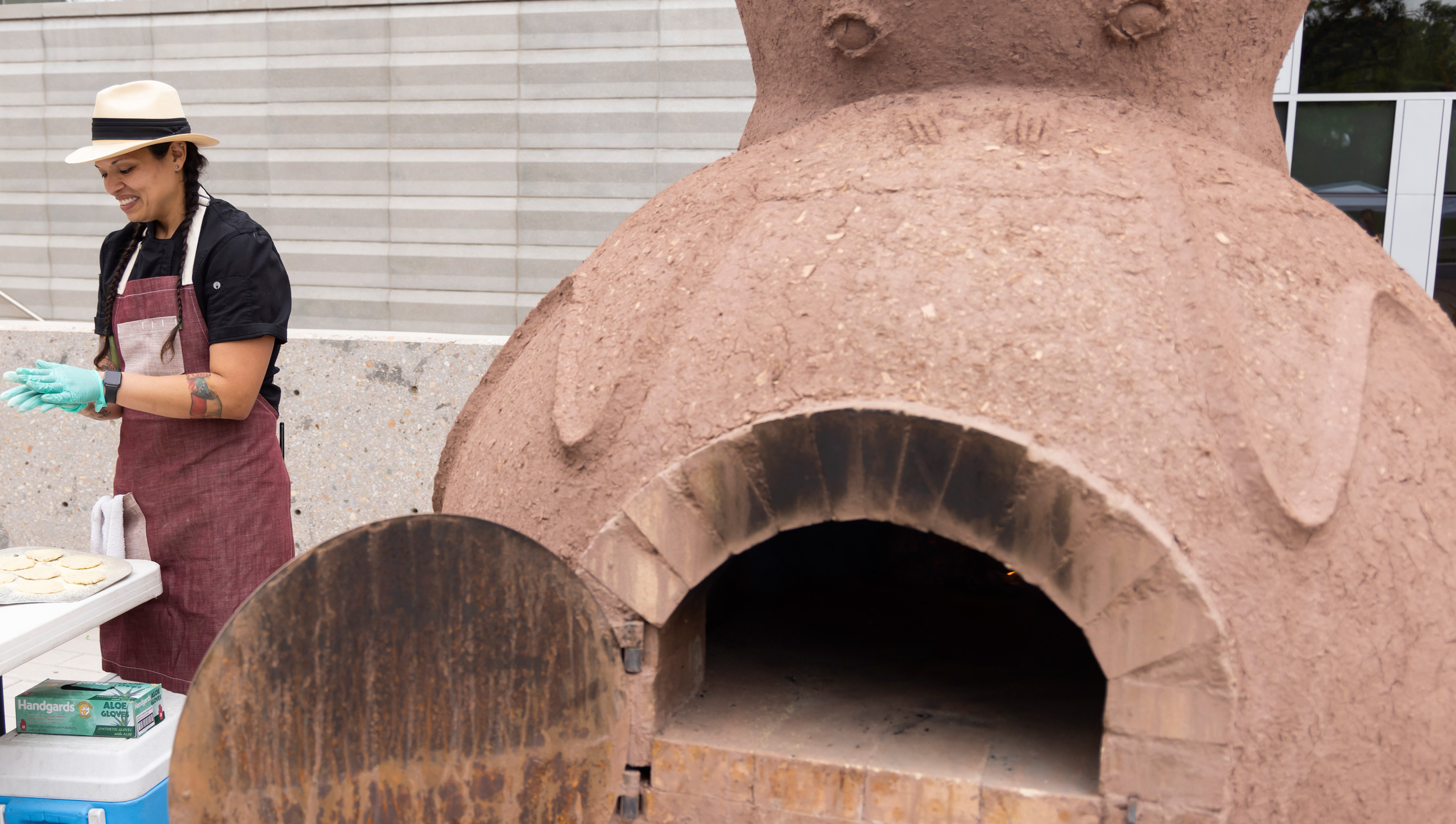 Chef Andrea Murdoch making flatbreads next to large ceramic oven outside the museum