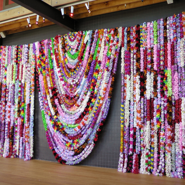 Installation view of a wall of dozens of leis sticthed together to form a tapestry