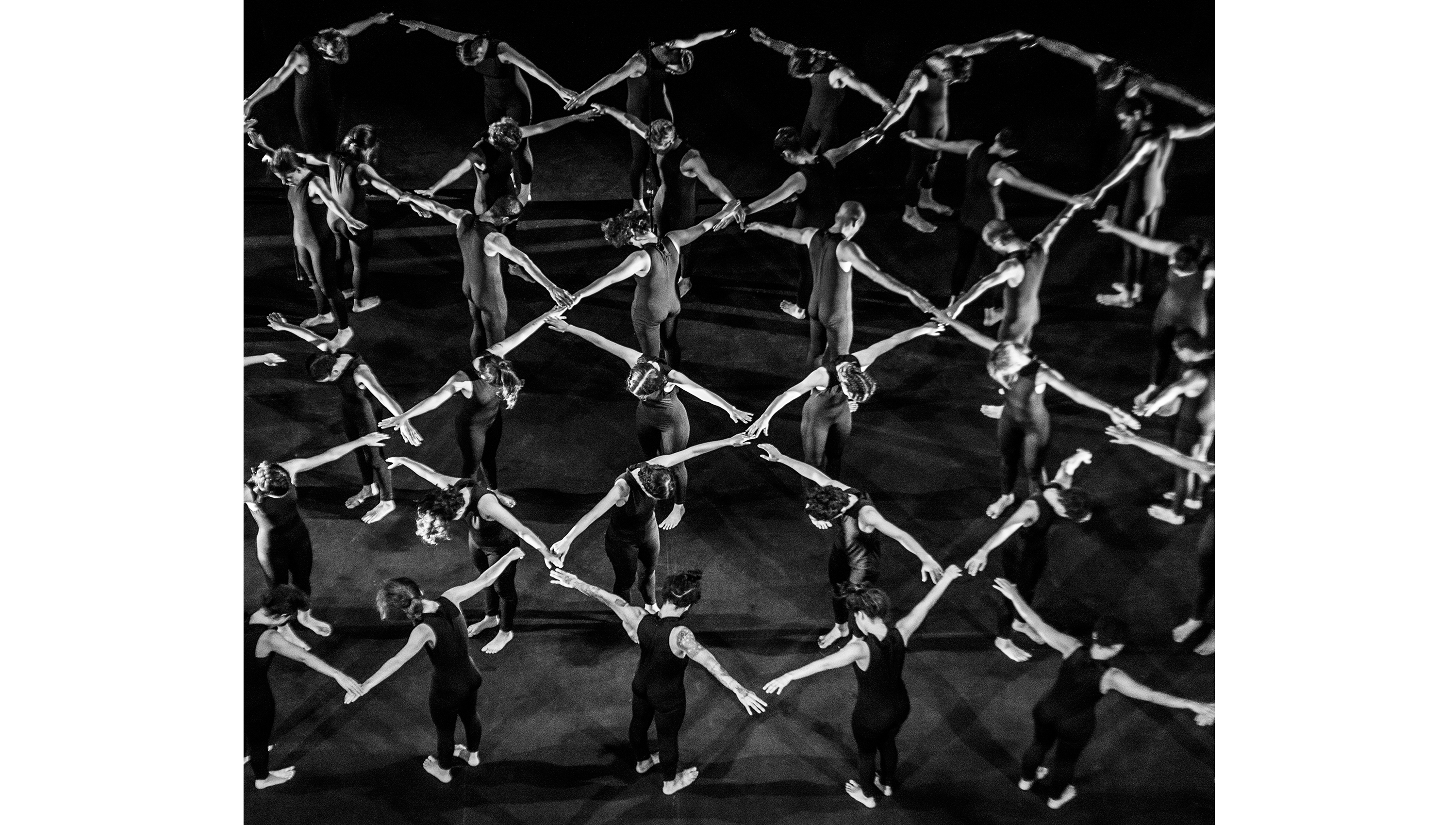 Black and white photograph of a group of dancers with their hands outstretched touching each other's