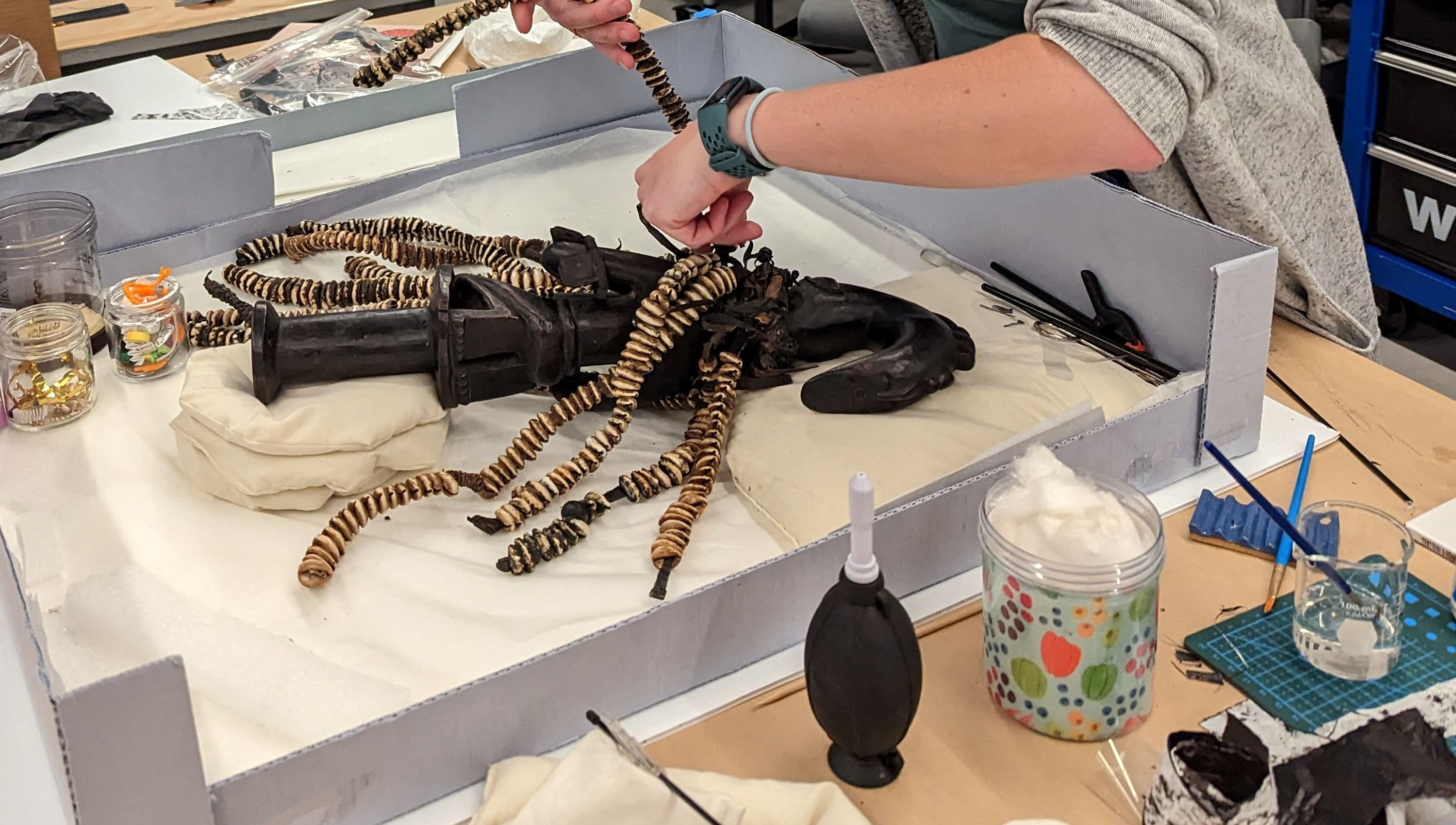 close up of Celine's hands working on Esu figure on a table in the conservation lab