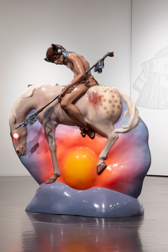 Set atop a purple, pink, and orange sunset, a white horse bucks its hind legs with an Indigenous person riding it bareback. The person wears a brown waist covering, a bison horned headpiece, and holds a spear. The horse has glowing red eyes and a bloody handprint on its rear end.