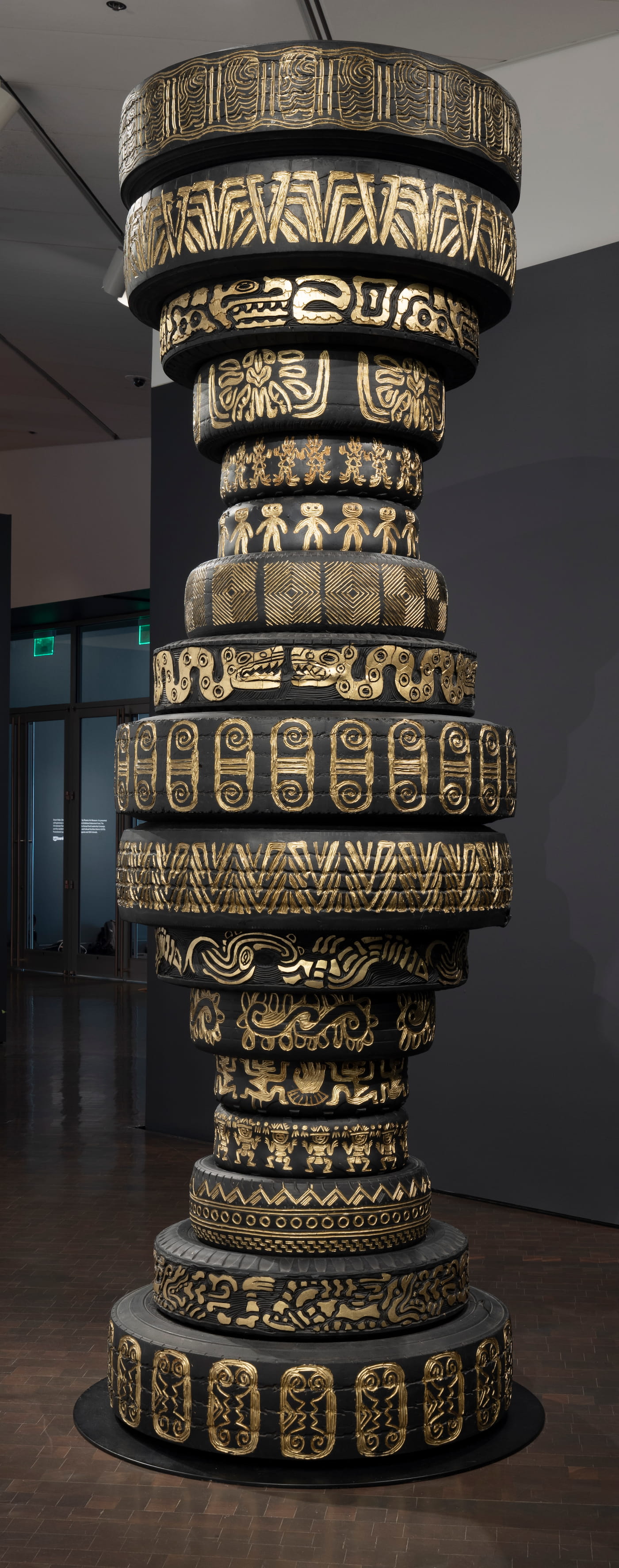 Standing over thirteen feet tall, a tower of stacked tires is shaped like two hourglasses on top of each other. The tower has different intricate painted gold symbols engraved on each tire.