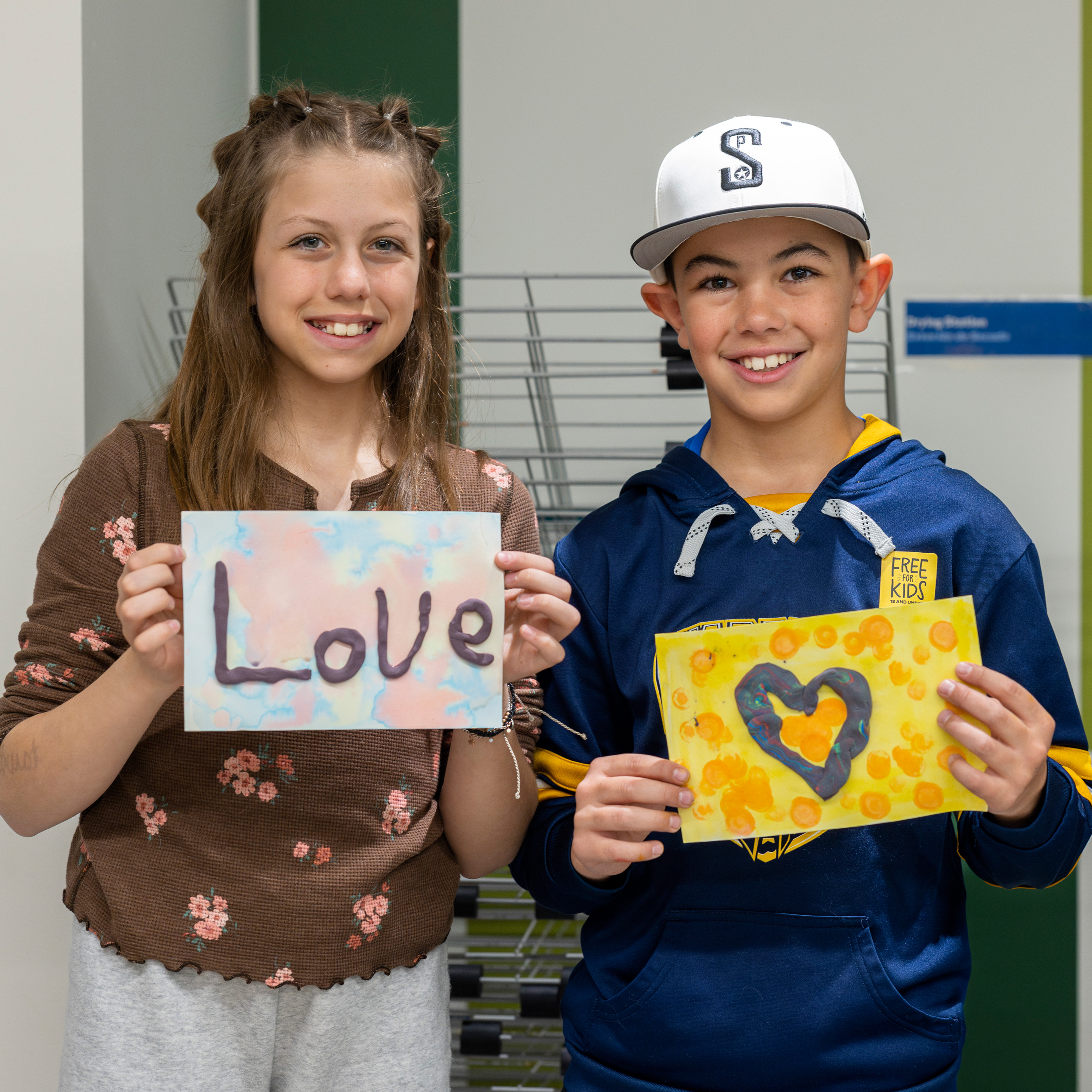 a girl holds an artwork that spells love and a boy holds a picture of a heart