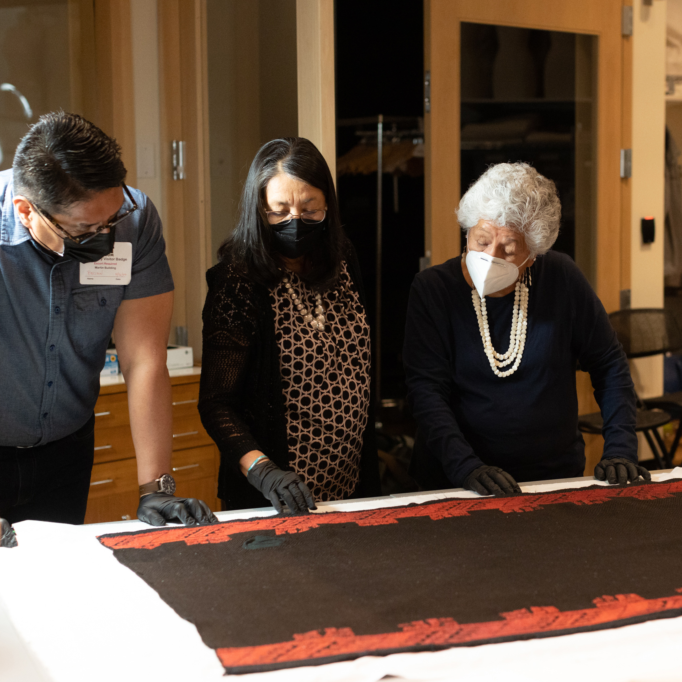 DAM staff and Acoma cultural advisors looking at a large cloth on a table in the textile conservation lab