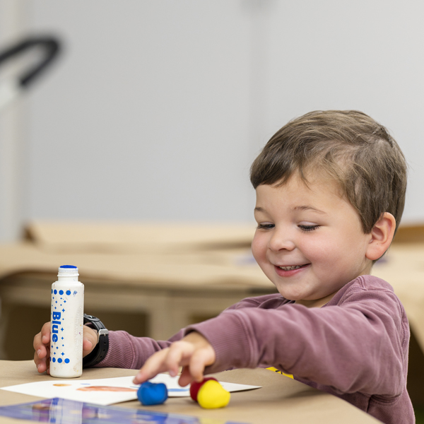 Young boy smiling and sitting at a table working on making art