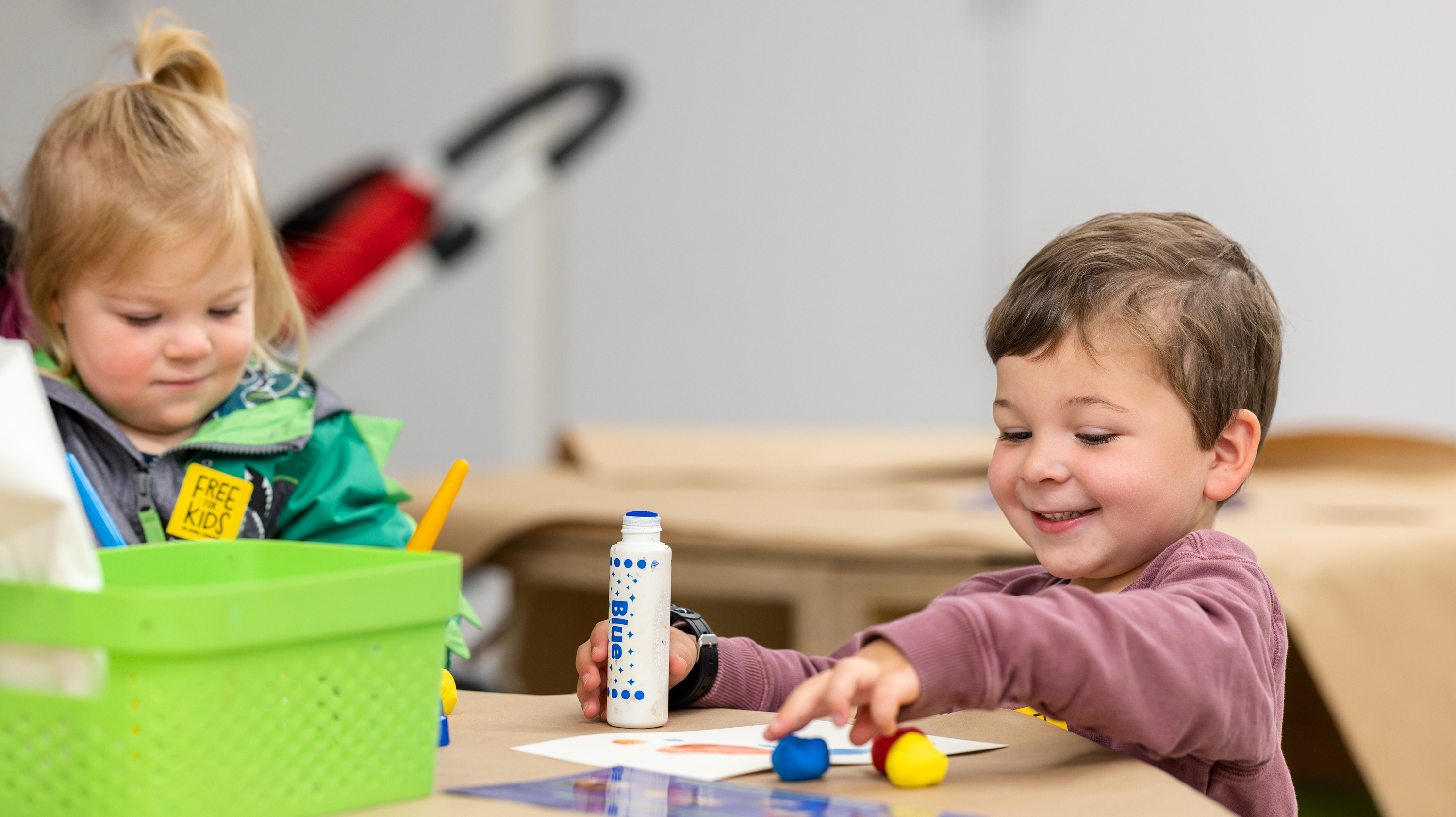 Two young kids sitting at a table working on making art together
