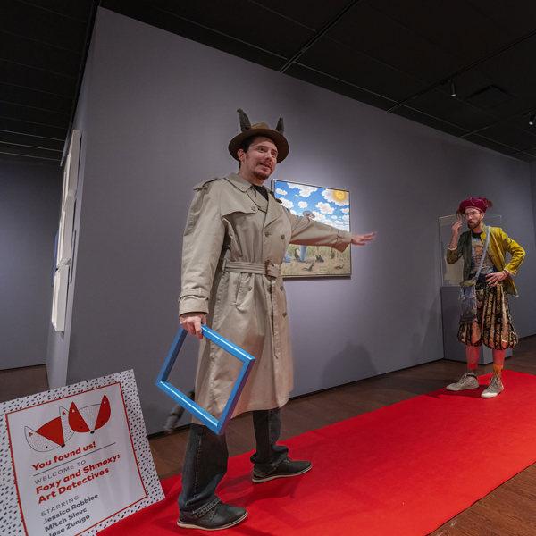 Man in a detective costume performing in front of a group of kids and adults in the galleries