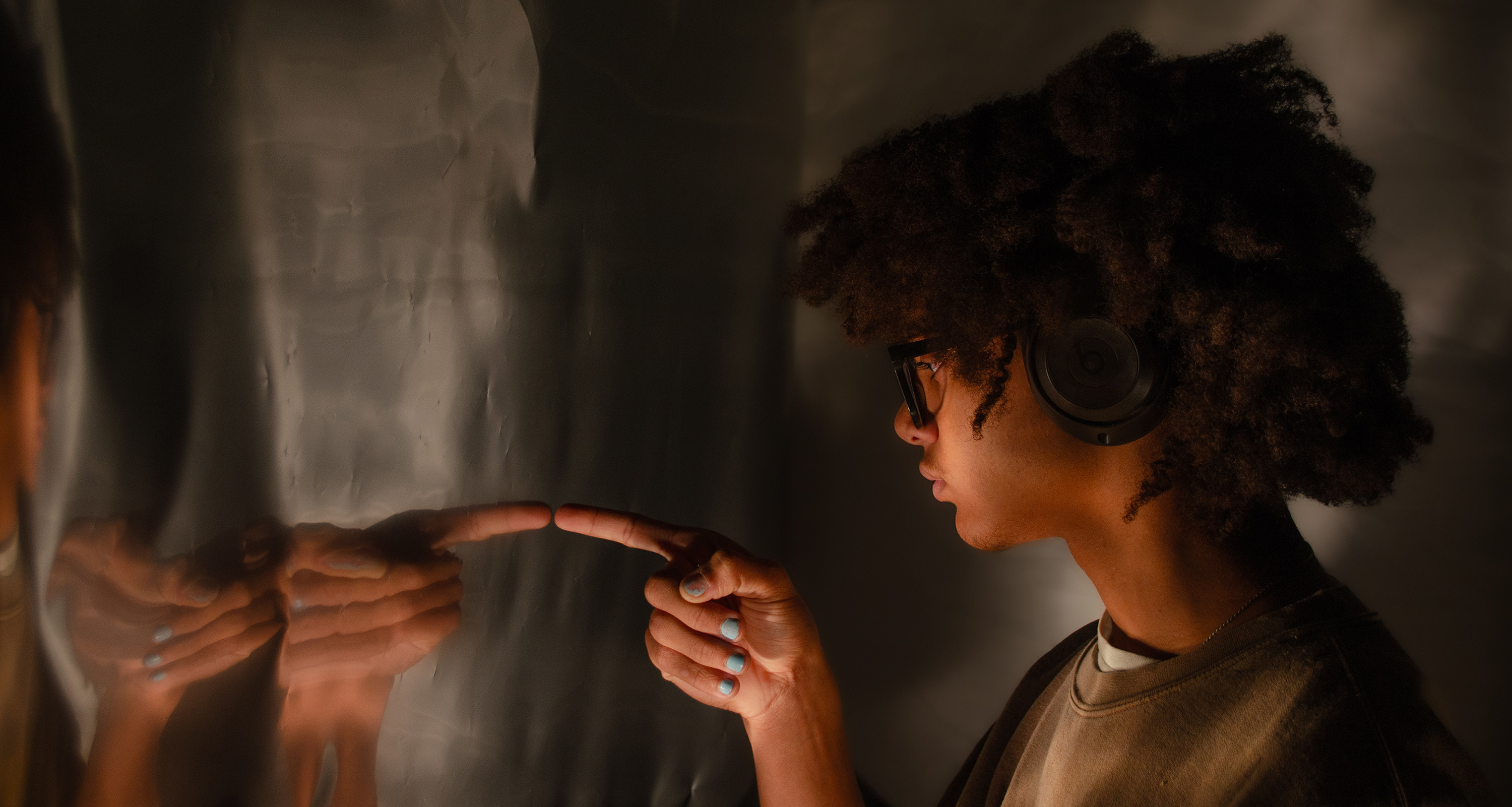 Young African American preteen with headphones on pointing at himself in a mirror
