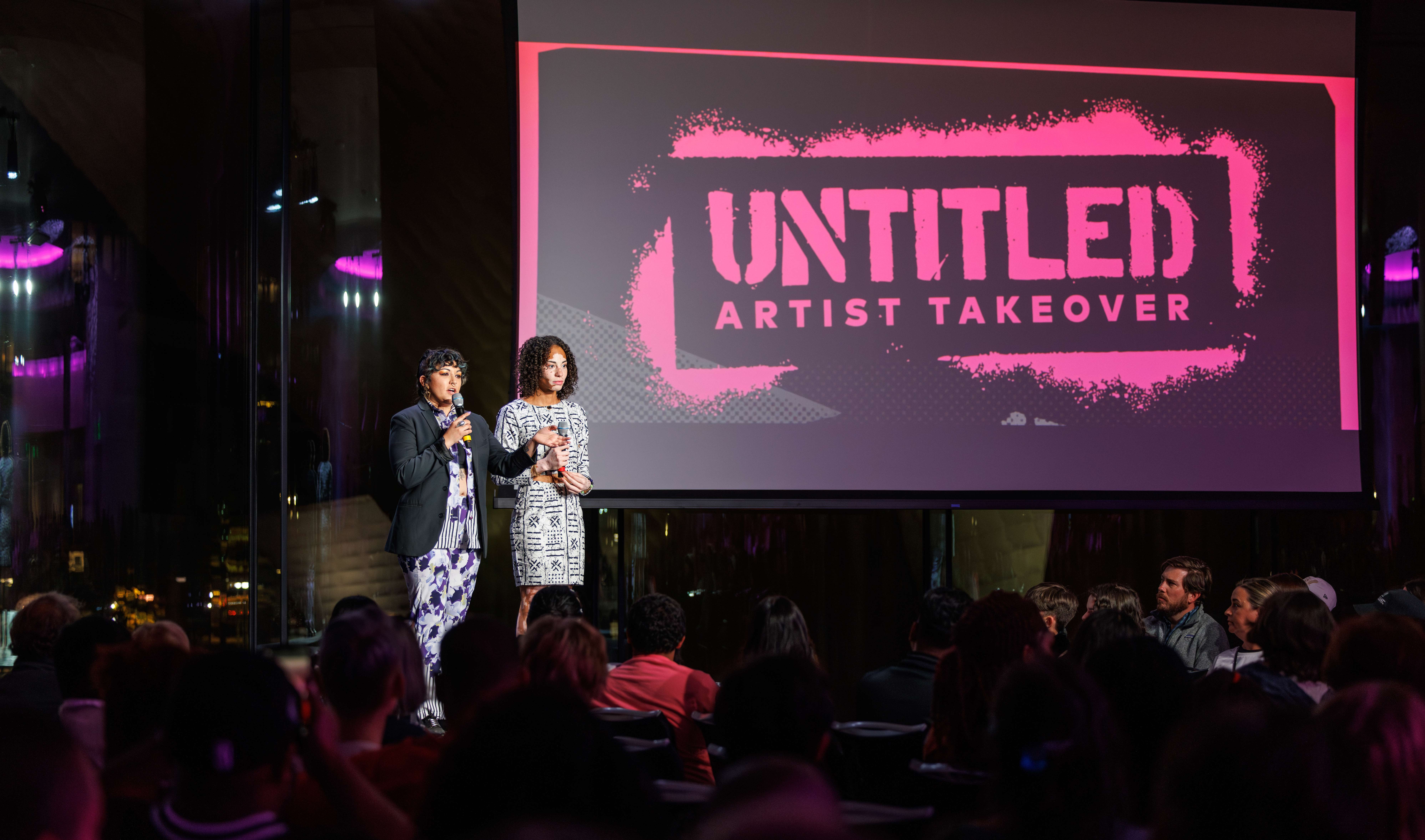 Two artists standing on stage in front of a large crowd at an after hours event at the museum