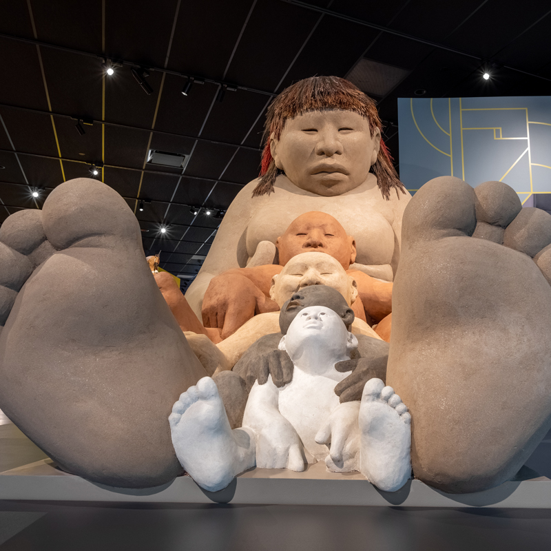 Large, tall clay sculpture in the shape of an Indigenous woman sitting down