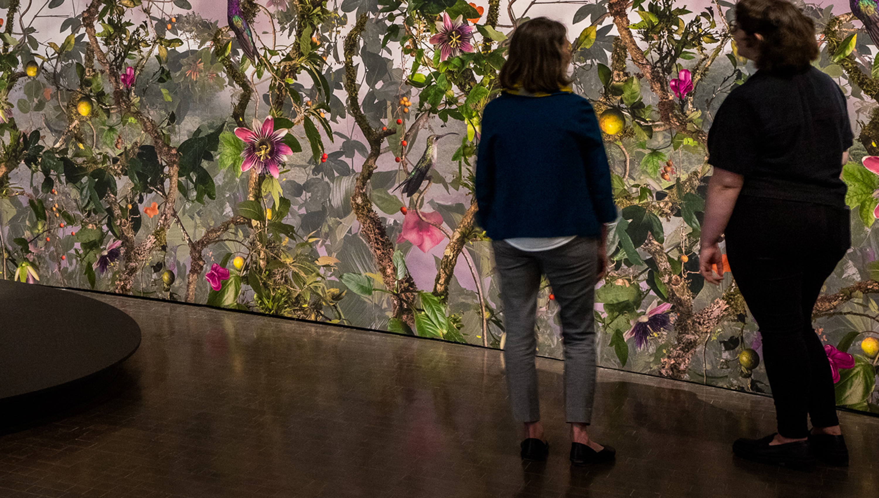 2 people in the Biophilia exhibition in front of a wall covered with green vines and pink flowers