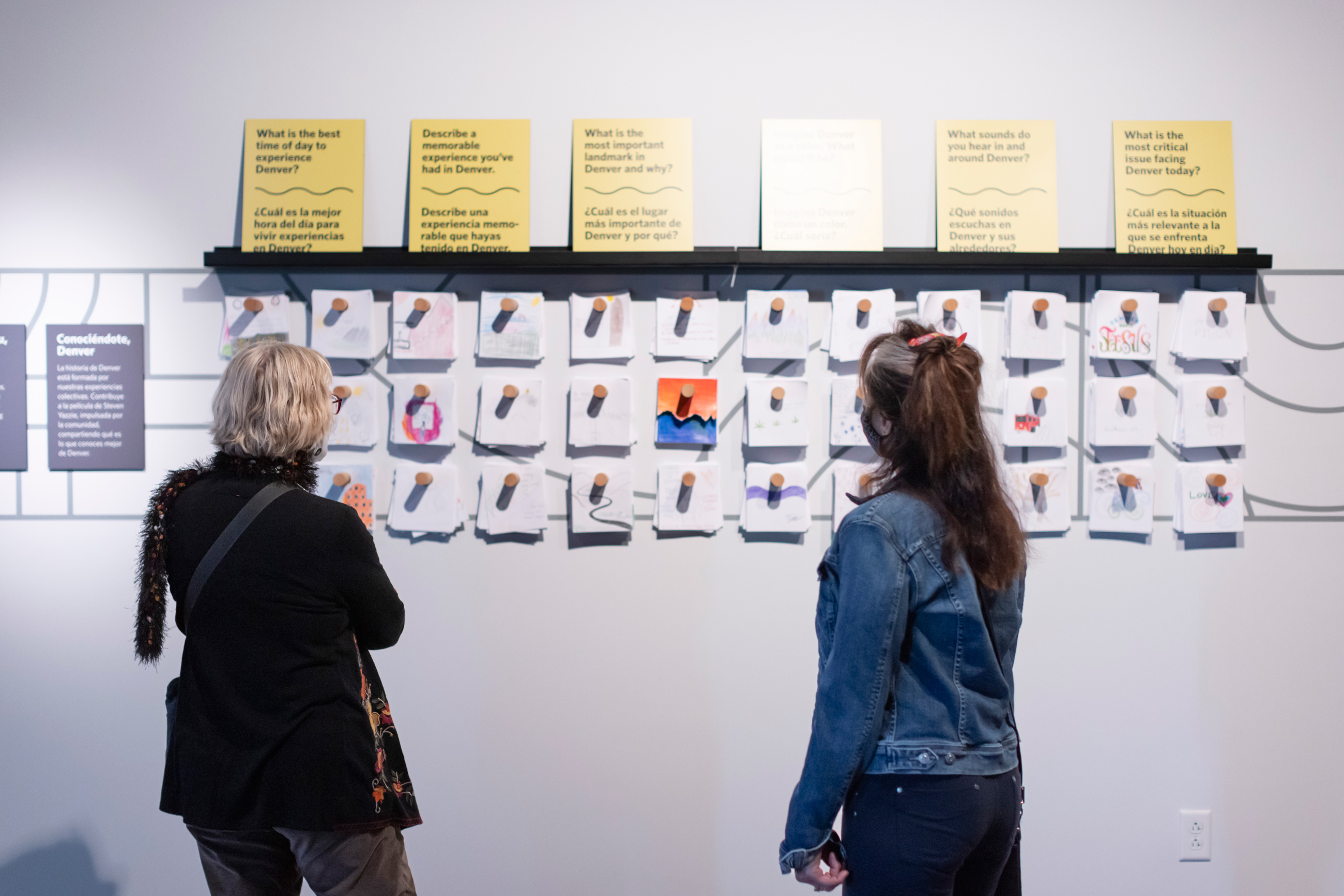 Two women examining a wall of words and postcards
