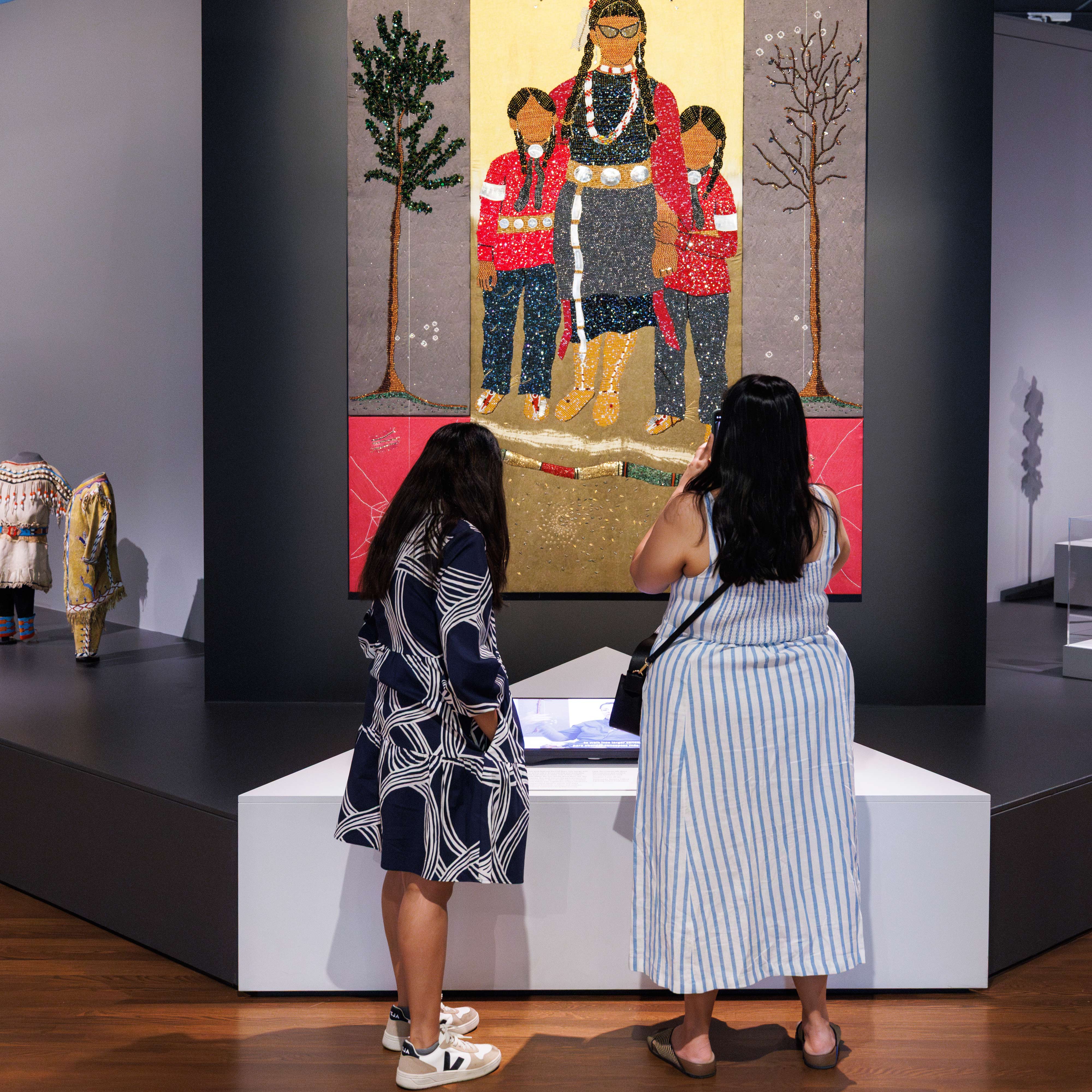 Two visitors taking a photo of a large Indigenous artwork