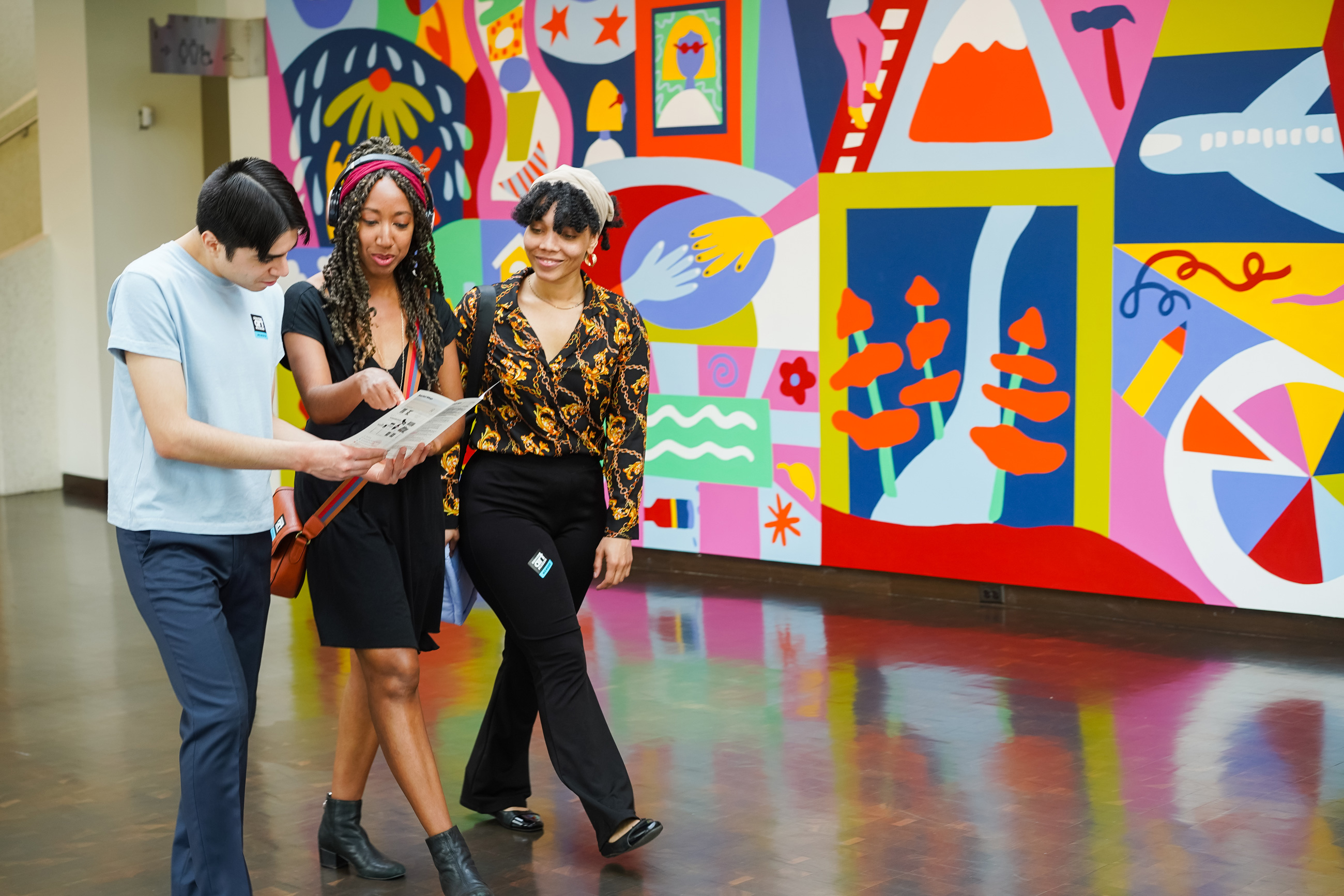 three people walking by a mural in the museum looking at a map and guide