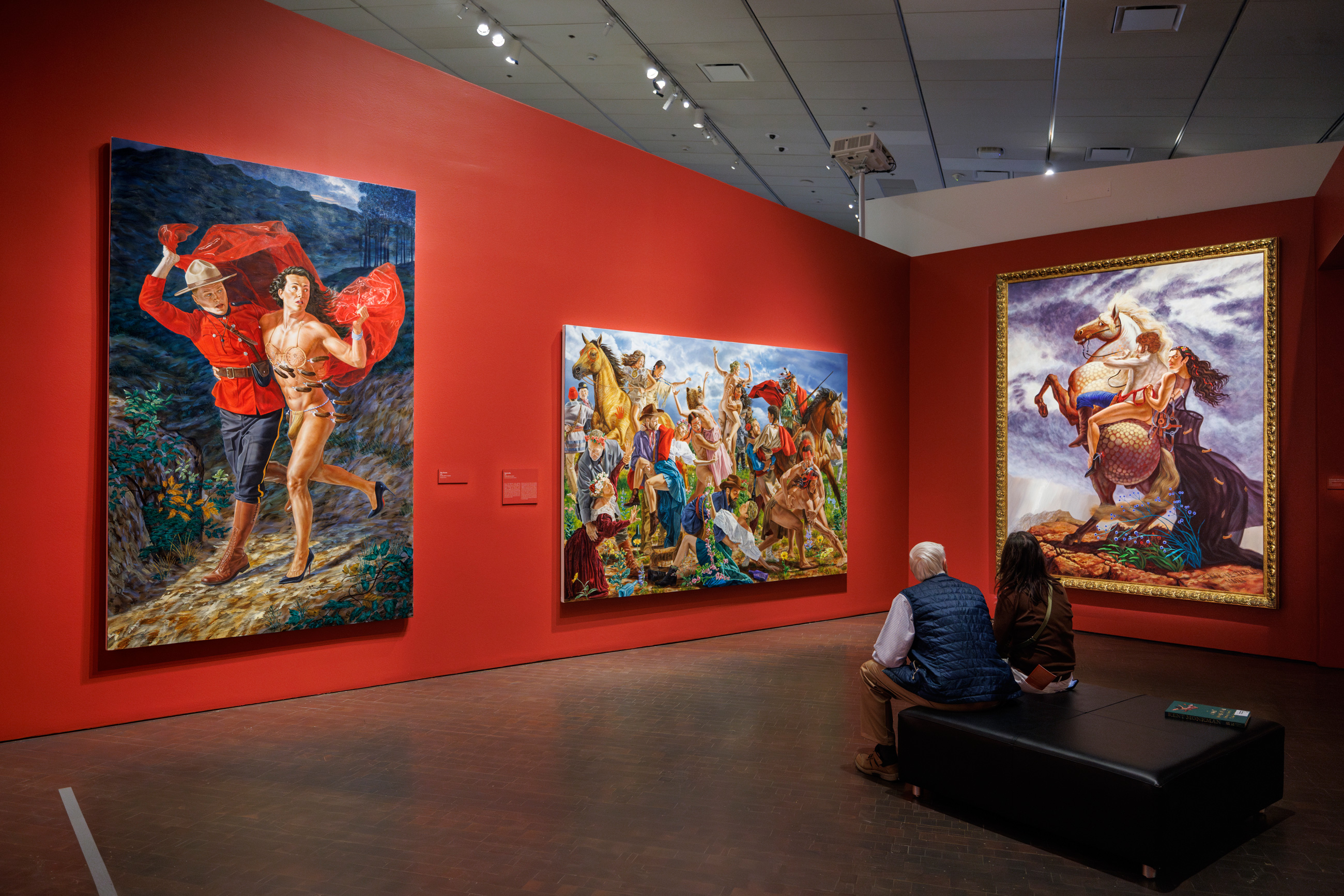 2 people sitting on an ottoman looking at paintings in the exhibition