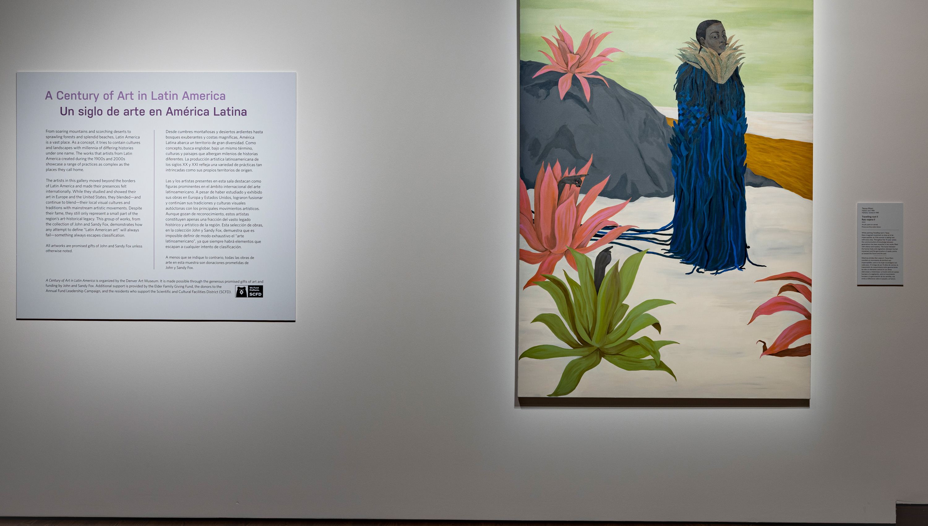 label text on the wall next to a painting of a woman in a blue garment in the middle of a fantastical landscape