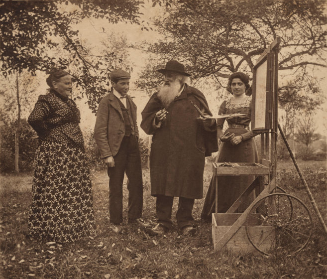 A black and white photo of a couple and their two teenage children in a forested area. They stand in front of an easel with a framed painting with the older man holding a paintbrush.