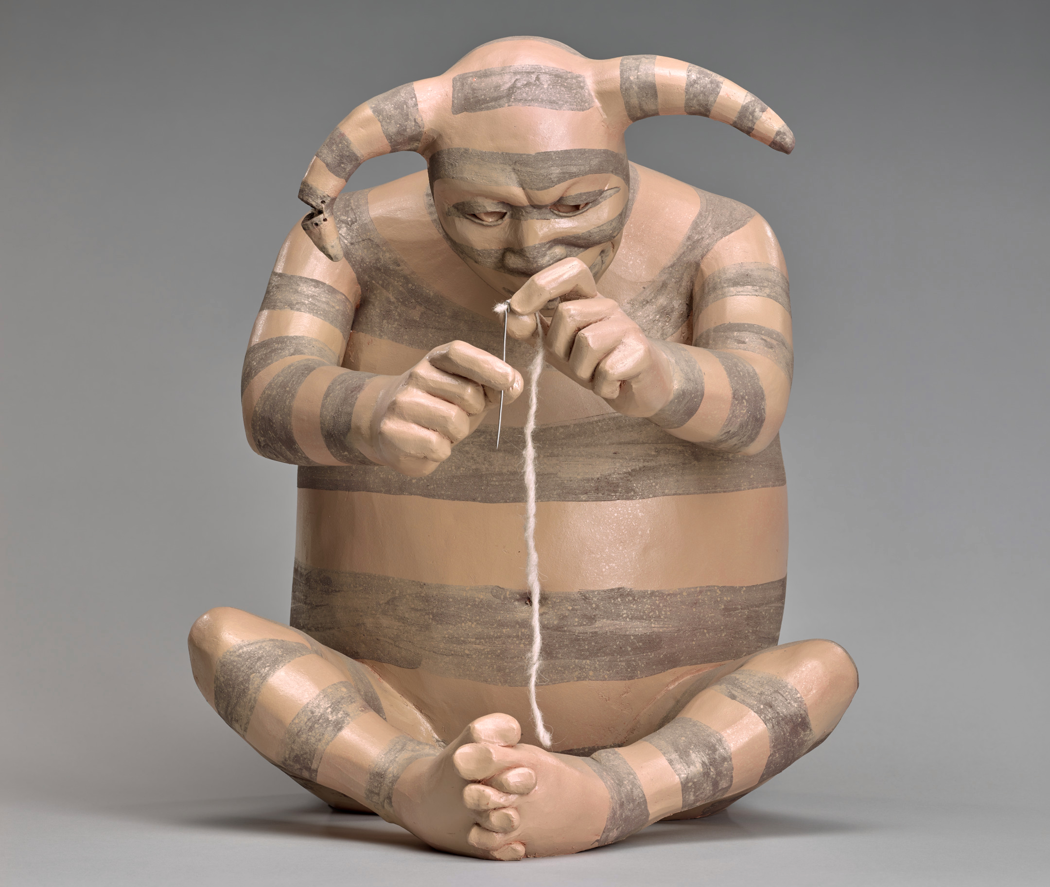 Small clay statue of a horned man-like figure working with a piece of string