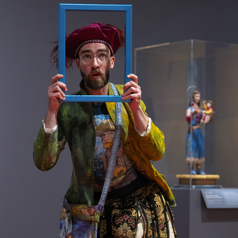 Man in a detective costume performing in front of a group of kids and adults in the galleries