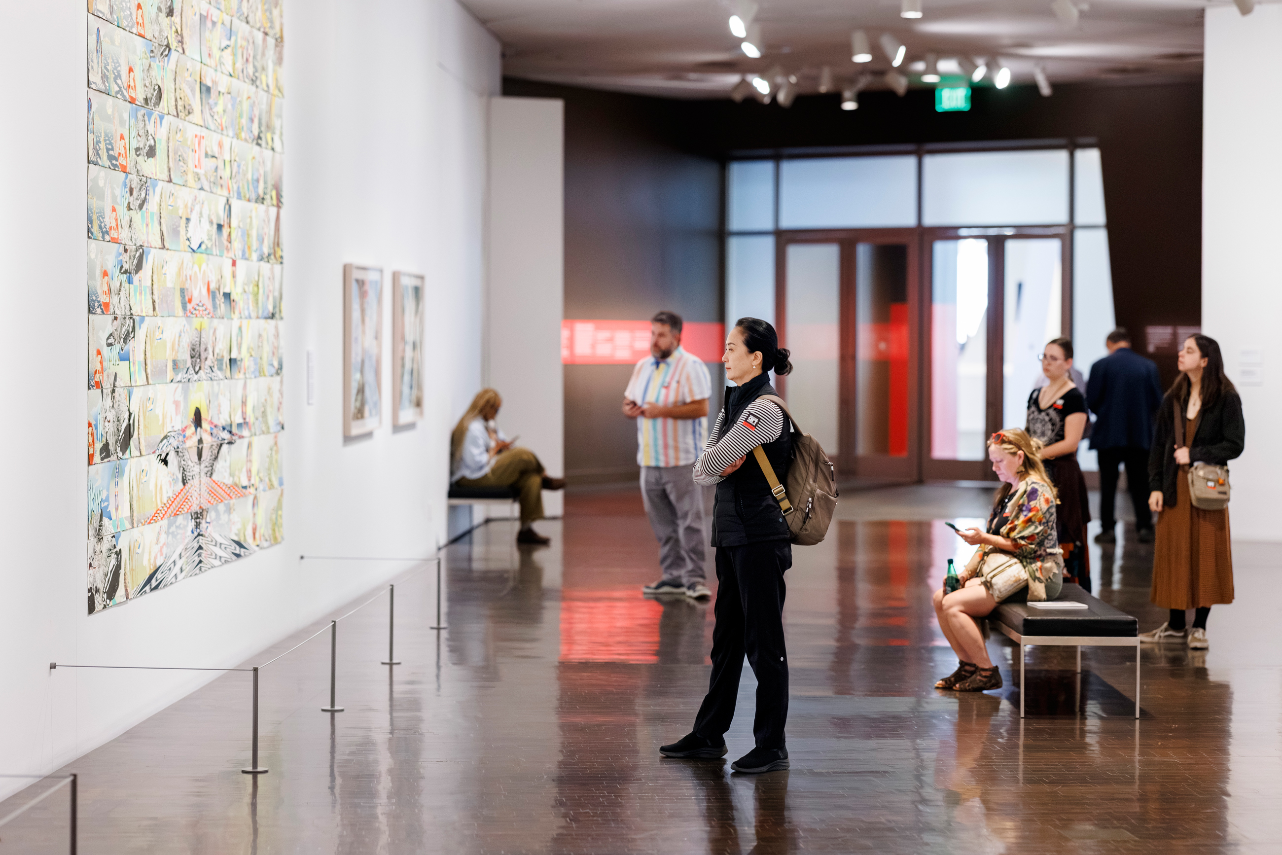 Wide shot of several visitors looking at art in the Andrea Carlson exhibition