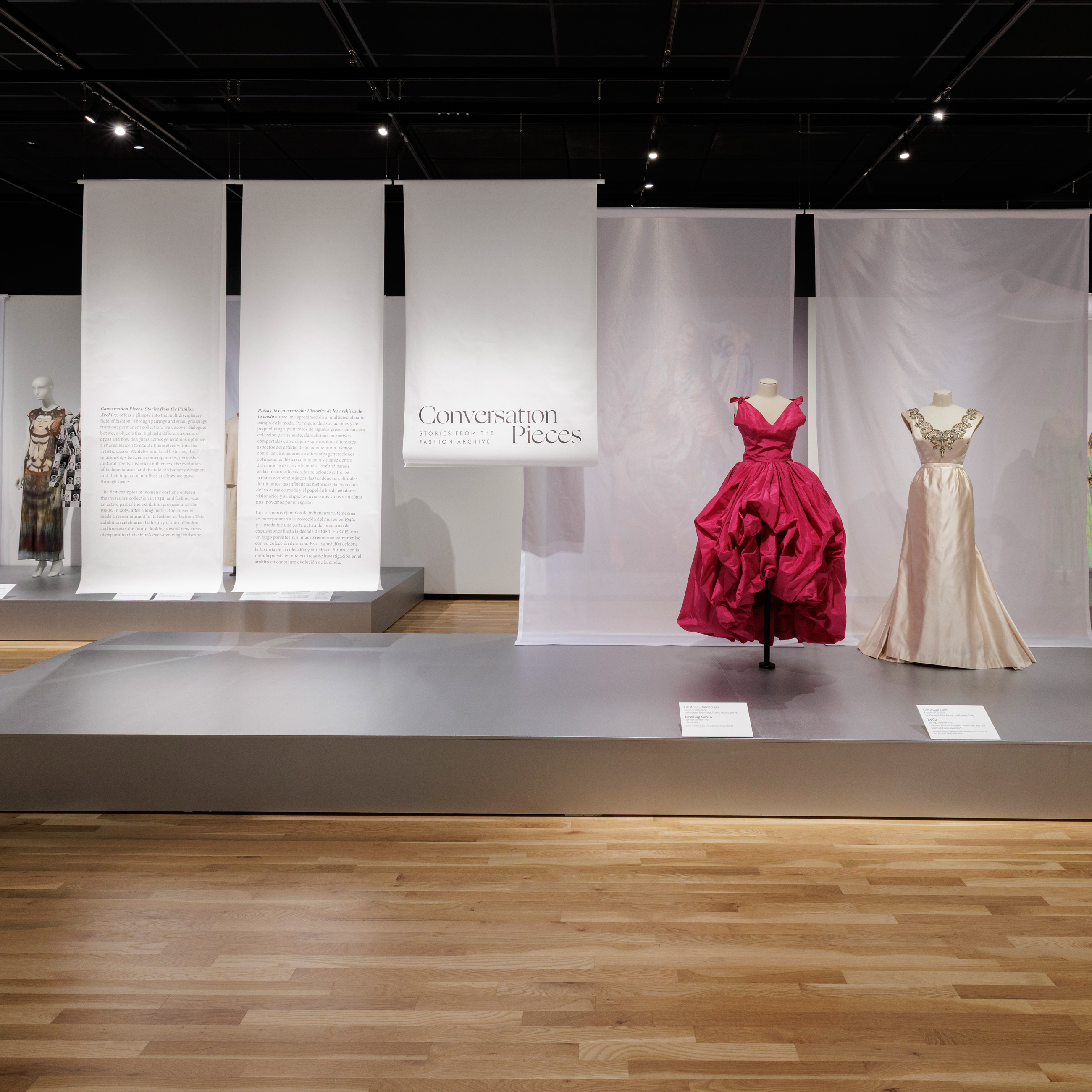 a bright pink dress and a white gown on display in Conversation Pieces