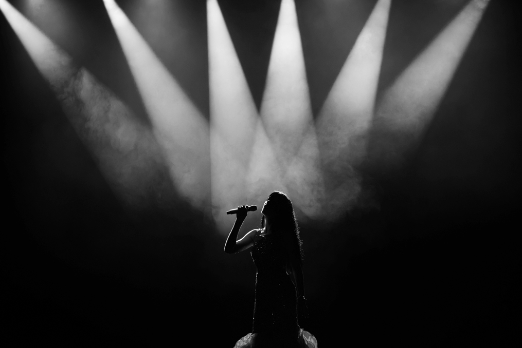 Black and white photo of a singer standing in the middle of a spotlight on stage