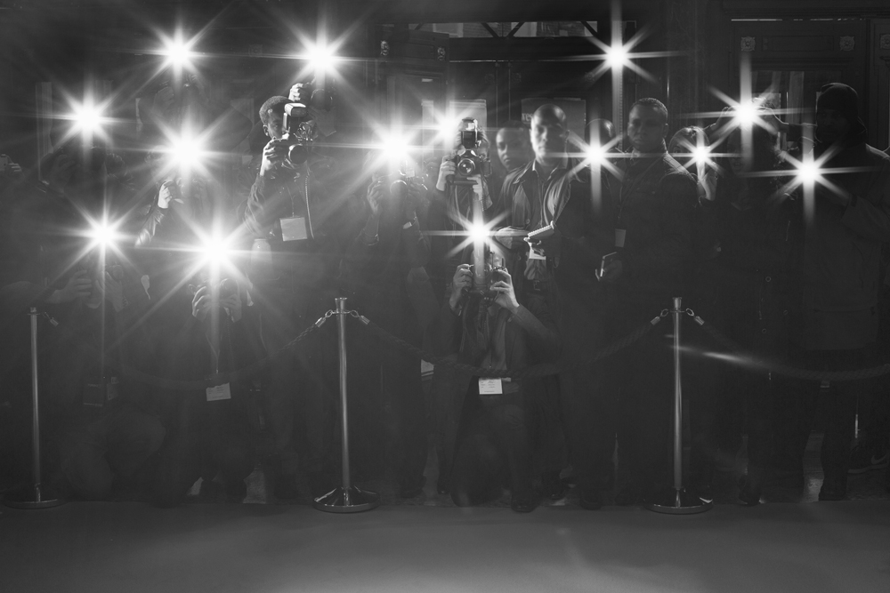 Black and white photo of a red carpet with cameras flashing