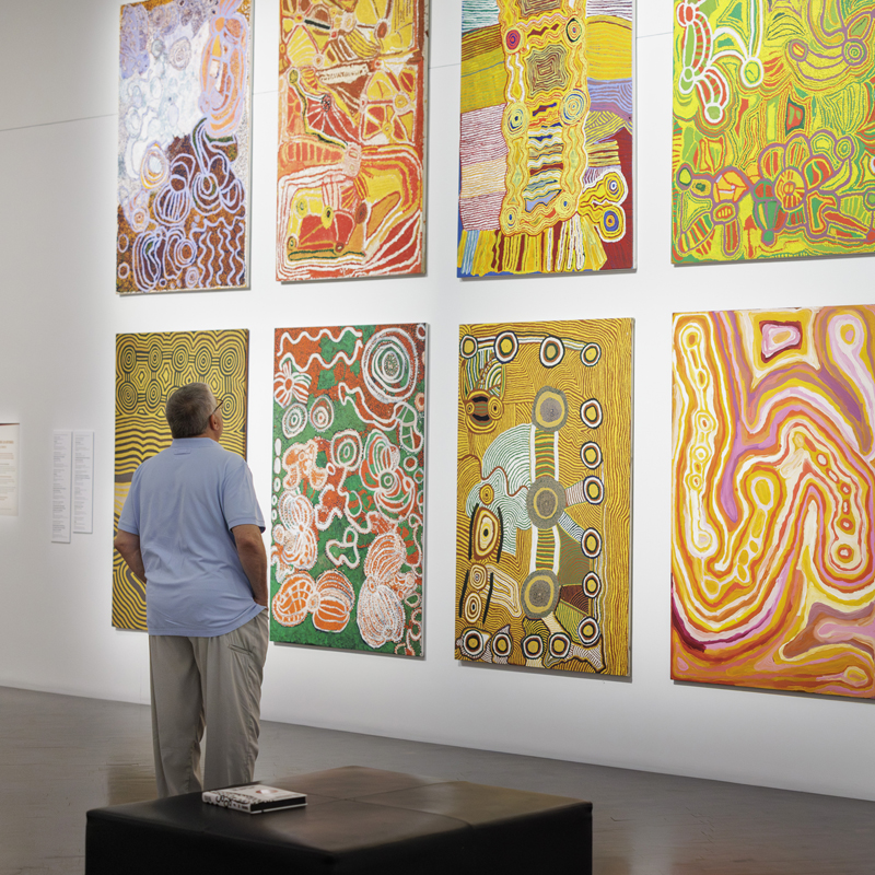 Man looking at a wall of colorful paintings