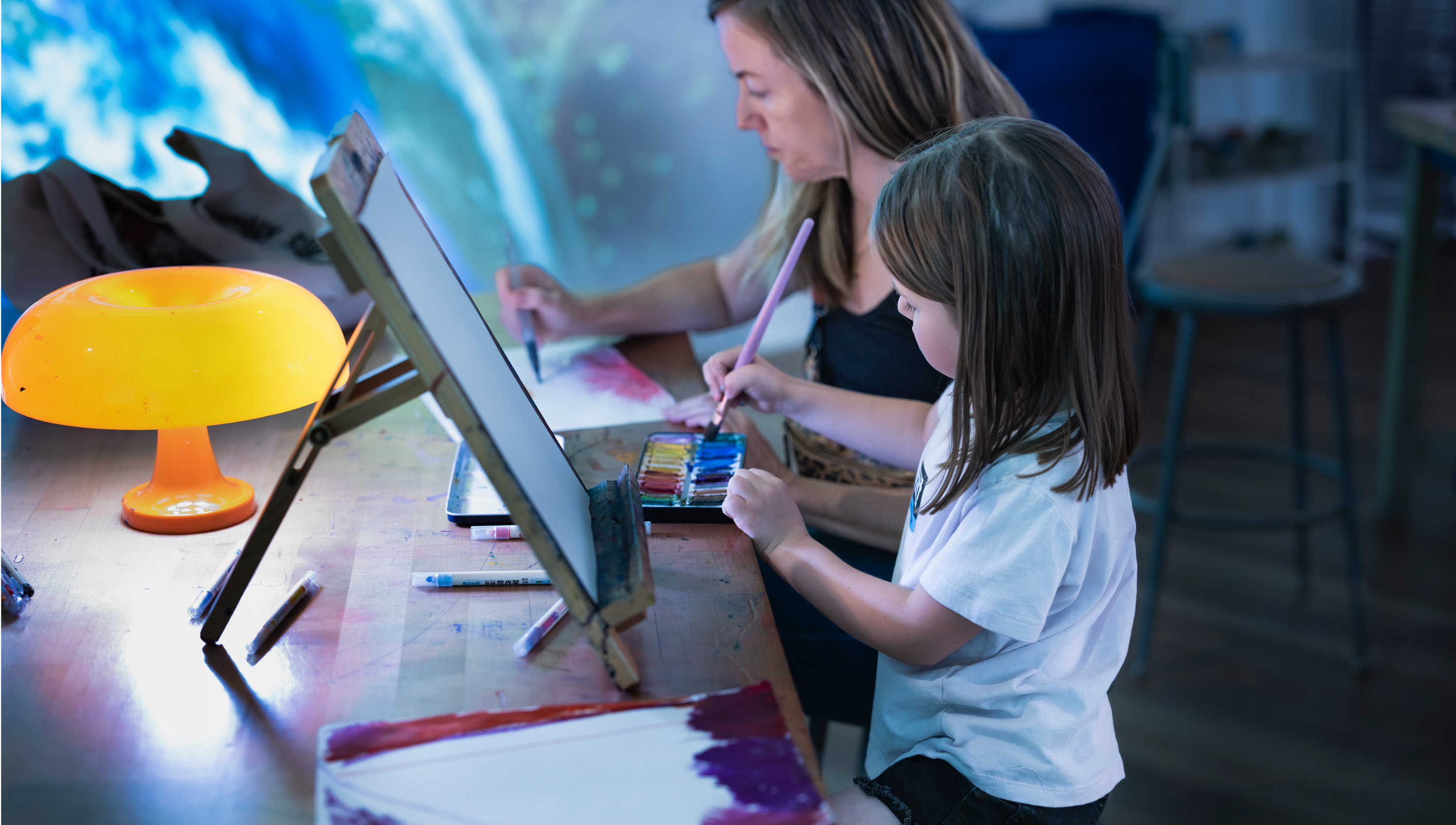 a mom and a child painting on papers on a table in the Cosmic Studio at the museum