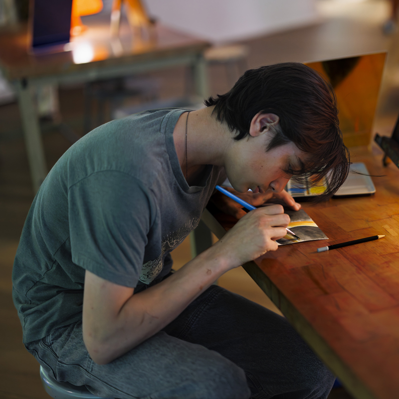Teen hunched over a table drawing with art utensils