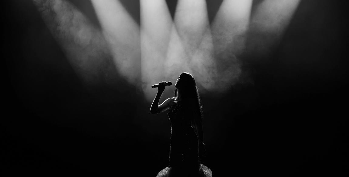 Black and white photograph of a singer on stage underneath multiple spotlights