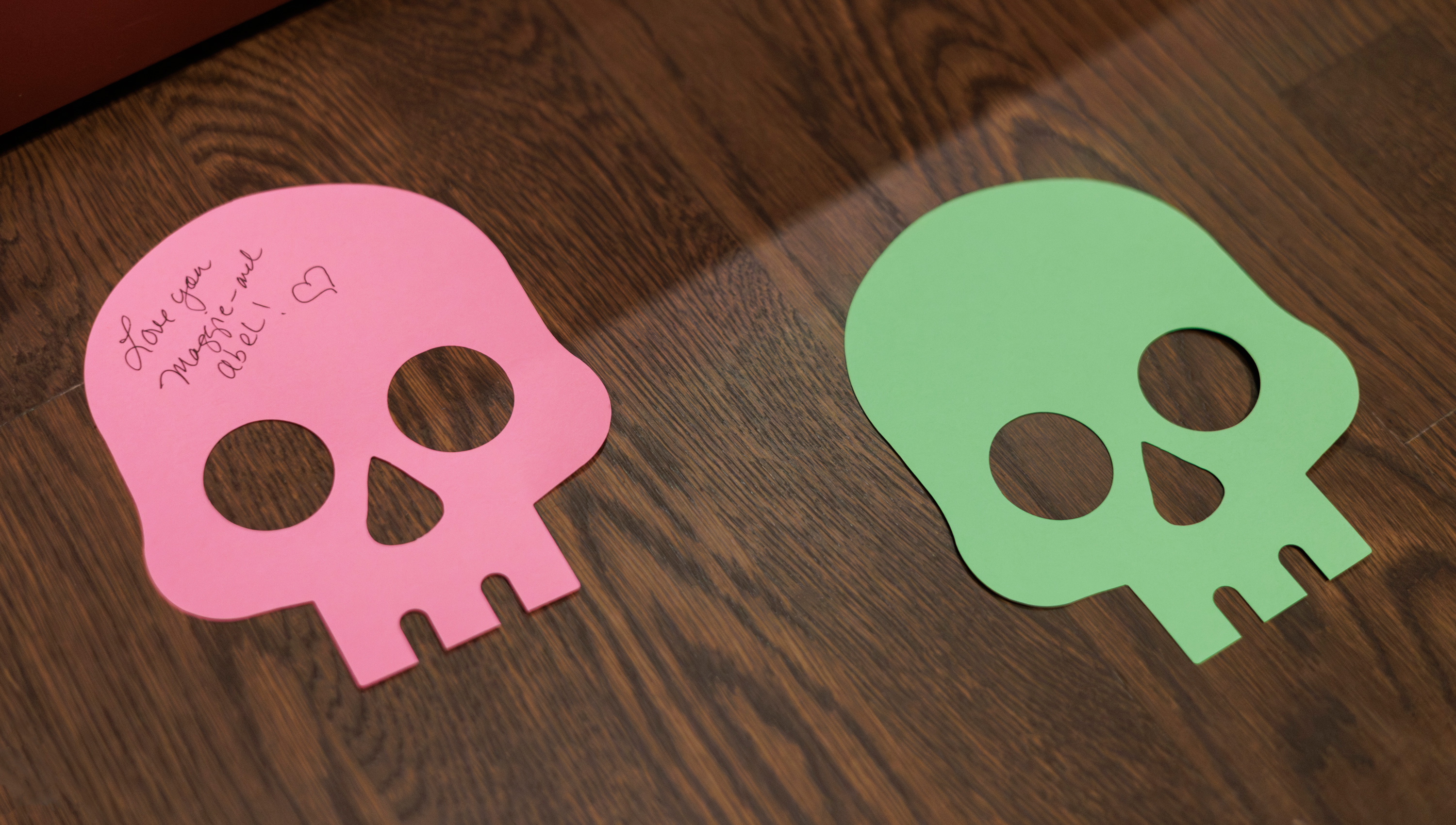 2 paper skulls on the floor. 1 has writing on it that says love you maggie and abel!